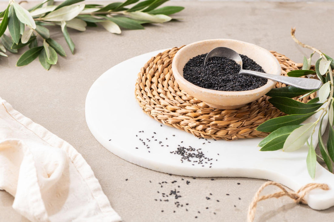 Black sesame seeds in a ceramic bowl with scattered seeds on a neutral background.
