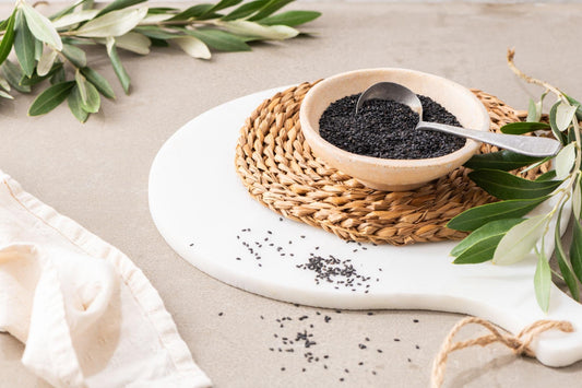 Black sesame seeds in a ceramic bowl with scattered seeds on a neutral background.