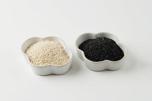     Black and white sesame seeds displayed side by side in white bowls.