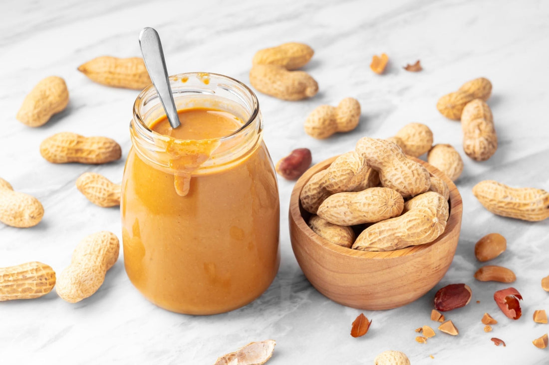 Creamy peanut butter in a glass jar surrounded by peanuts