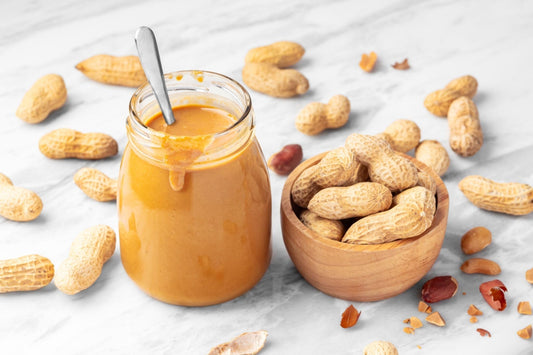 Creamy peanut butter in a glass jar surrounded by peanuts