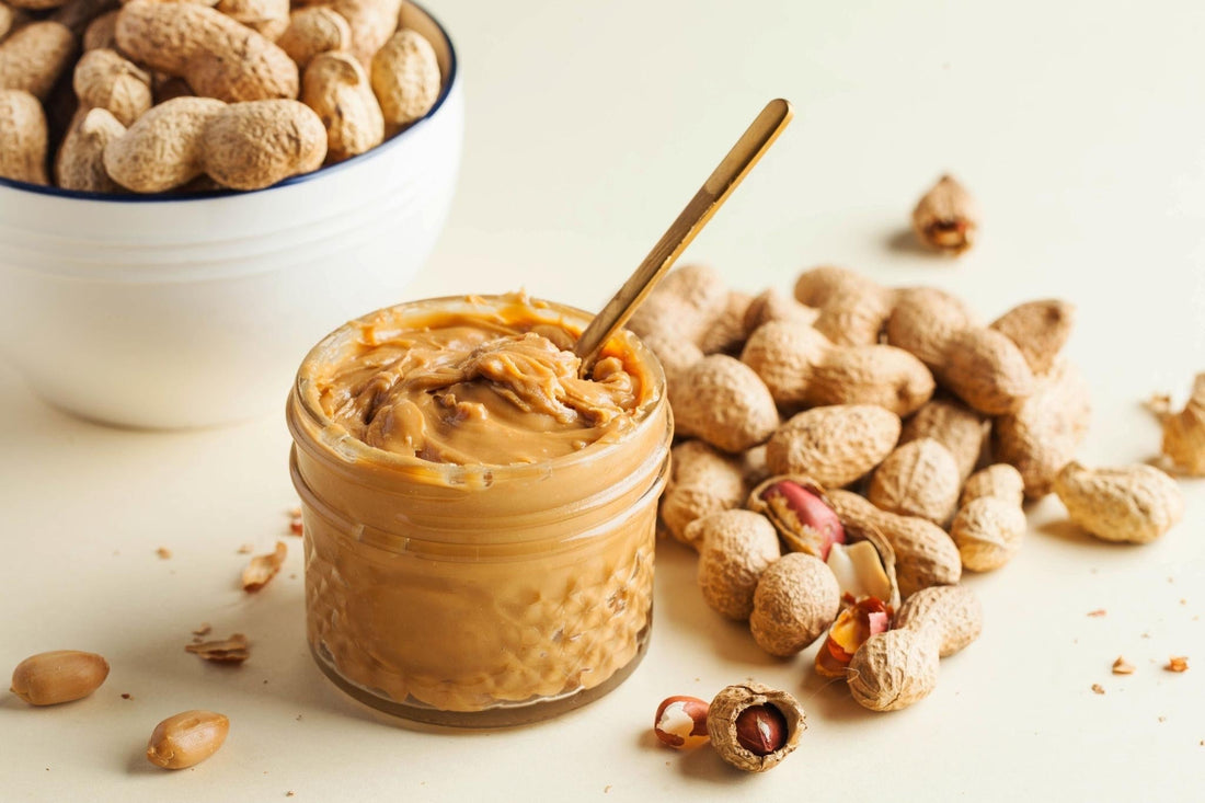 Homemade peanut butter in a glass jar with peanuts and a spoon