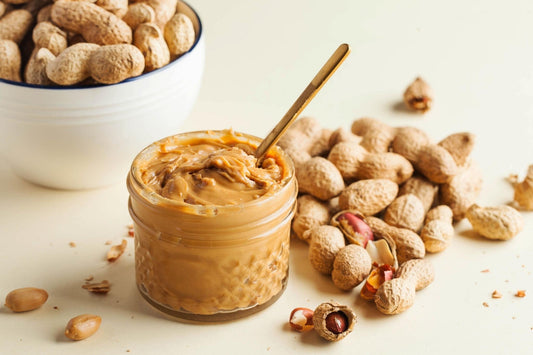 Homemade peanut butter in a glass jar with peanuts and a spoon