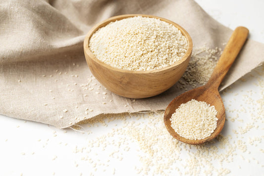 White sesame seeds in a wooden bowl with a wooden spoon on a neutral linen background