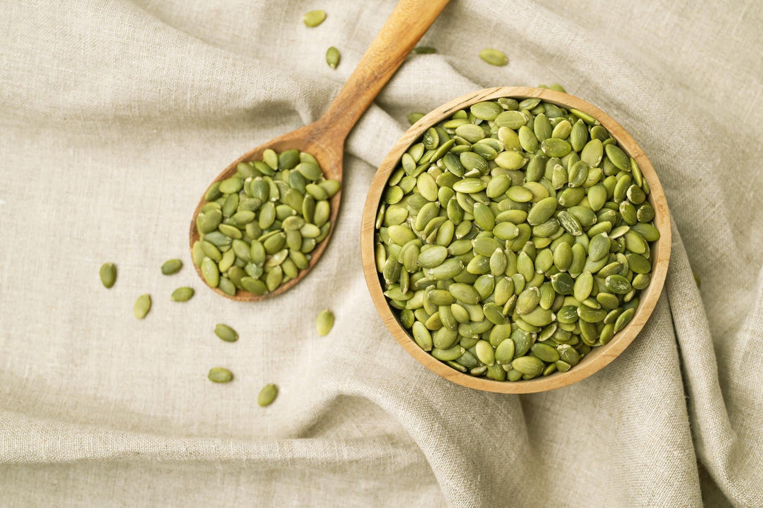  Pumpkin seeds in a wooden bowl with scattered green pumpkin seed kernels