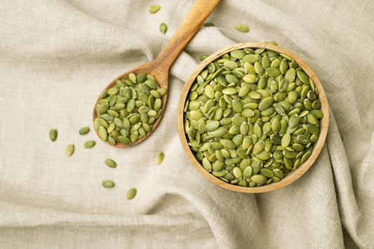  Pumpkin seeds in a wooden bowl with scattered green pumpkin seed kernels